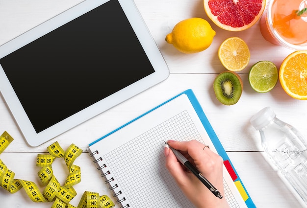 Photo fresh juice in glass from citrus fruits  lemon grapefruit orange notebook with pencil on white woode...