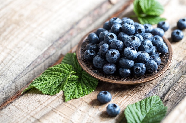 fresh juicy blueberries with green leaves in a plate on a wooden table. healthy berry, antioxidants, antiage foods