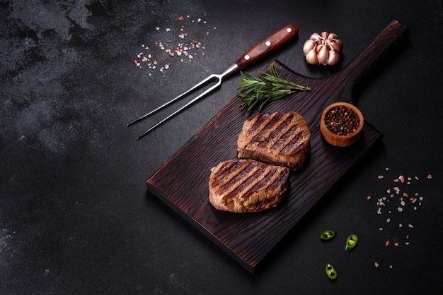 Fresh juicy delicious beef steak on a dark background. Meat dish with spices and herbs