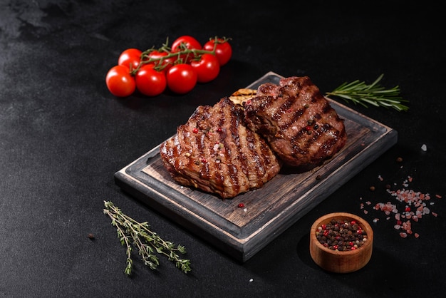 Fresh juicy delicious beef steak on a dark surface. Meat dish with spices and herbs