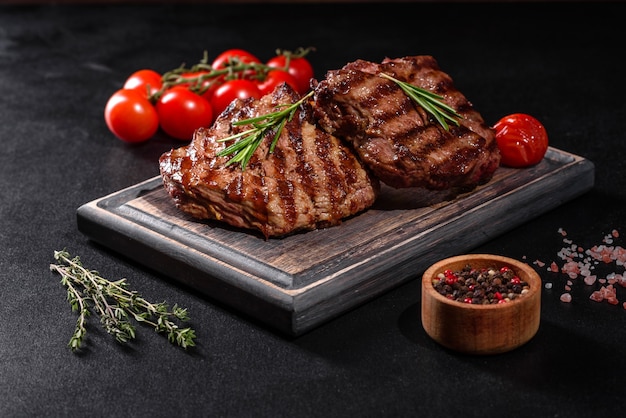 Fresh juicy delicious beef steak on a dark table. Meat dish with spices and herbs