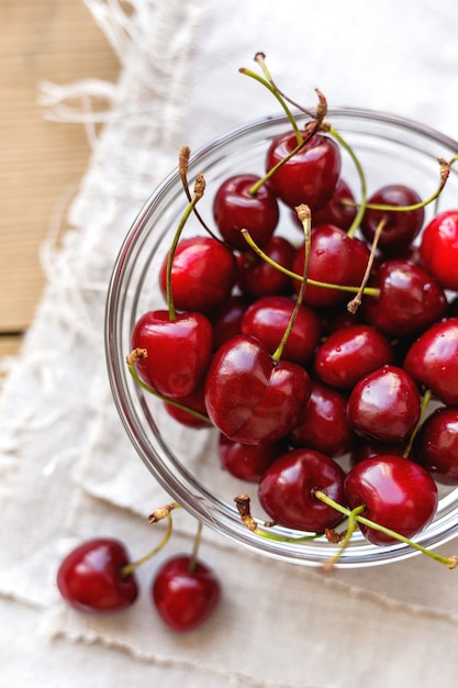 Fresh juicy sweet cherries in glass bowl. Rustic background with homespun napkin.