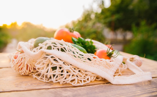 Fresh juicy vegetables products in a reusable shopping bag a string bag made of recycled materials on a wooden table in the garden Vegetarianism No plastic Ecofriendly lifestyle