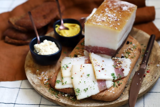 Fresh lard with meat layer on a wooden board with spices mustard and horseradish Delicious snack Bacon