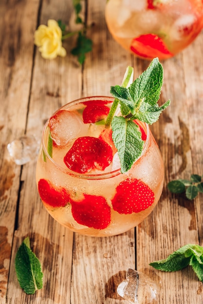 Fresh lemonade with green tea lime mint and strawberry on wooden background cold summer drink two glasses with berry ice tea selective focus