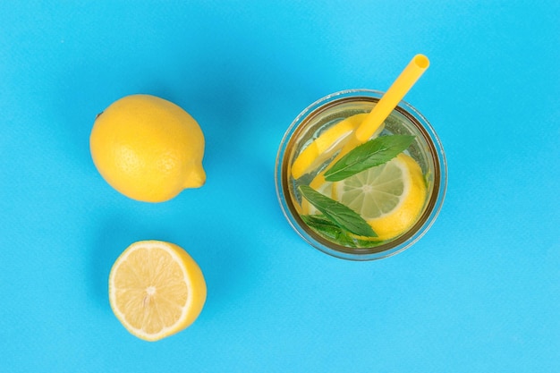 Fresh lemons and a glass of refreshing lemonade on a blue background