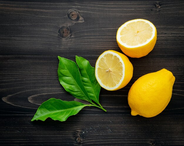 Fresh lemons and  lemons leaves on dark wooden background.