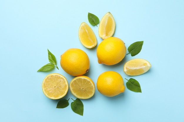 Fresh lemons with leaves on blue table, top view. Ripe fruit