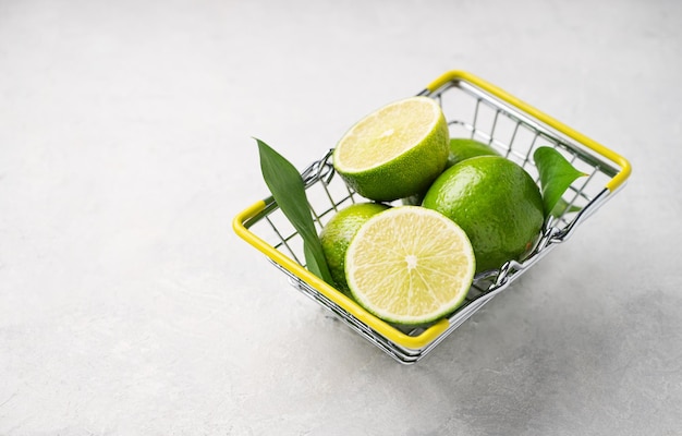 Fresh limes in a supermarket basket on a light textured background Citrus fruit concept for freshly squeezed lime mojito Copy space