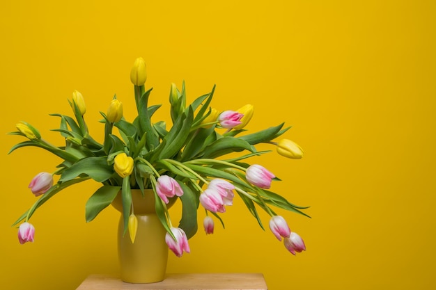 Fresh lush bouquet of pink yellow tulips on a yellow background With copy space