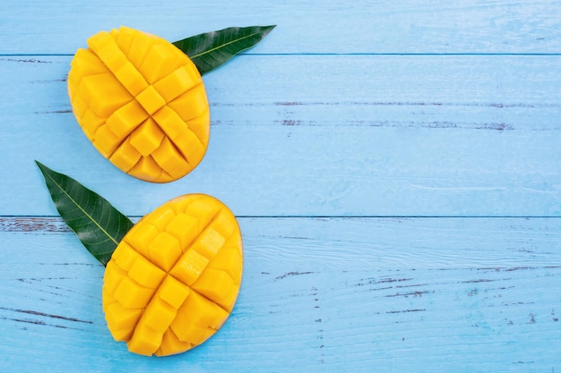 Fresh mango beautiful chopped fruit with green leaves on bright blue timber background Tropical fruit design concept Flat lay Top view Copy space