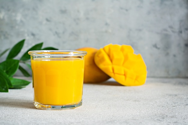 Fresh mango juice in a glass glass with mango slice on a gray background