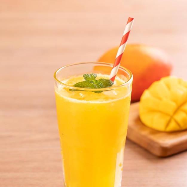 Fresh mango juice with beautiful chopped pulp flesh on bright wooden table background Tropical fruit drink design concept Close up copy space