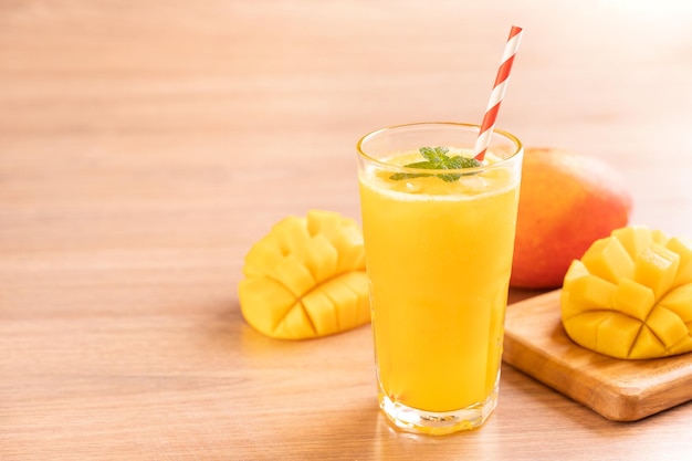 Fresh mango juice with beautiful chopped pulp flesh and straw on bright wooden table background Tropical fruit design concept Close up copy space