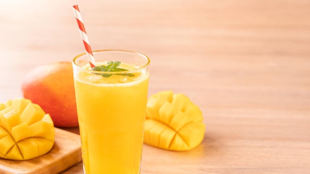 Fresh mango juice with beautiful chopped pulp flesh and straw on bright wooden table background Tropical fruit design concept Close up copy space