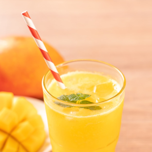 Fresh mango juice with beautiful chopped pulp flesh and straw on bright wooden table background