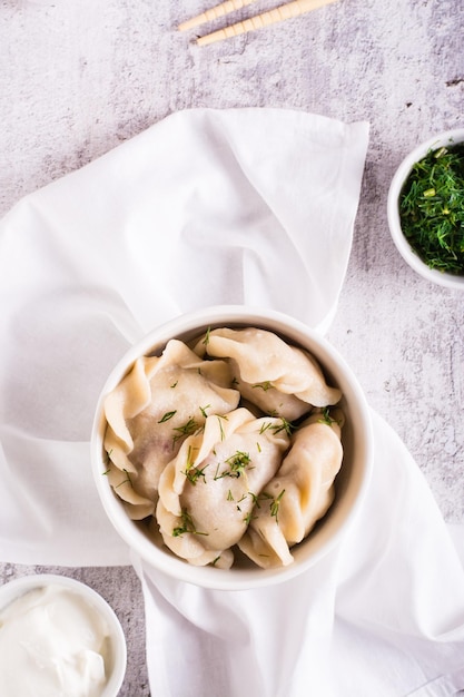 Fresh meat dumplings in a bowl with sour cream and herbs Homemade food Top and vertical view