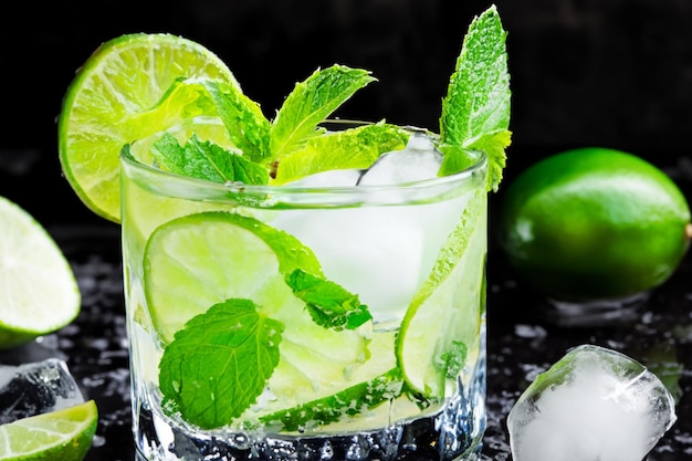 Fresh mojito drink with lime mint leaves and ice on black background