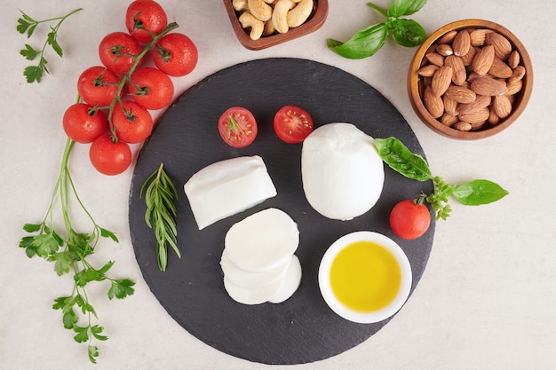 Fresh mozzarella cheese, Soft italian cheeses, tomato and basil, olives oil and rosemary on wooden serving board over light surface. Healthy food. Top view. Flat lay.