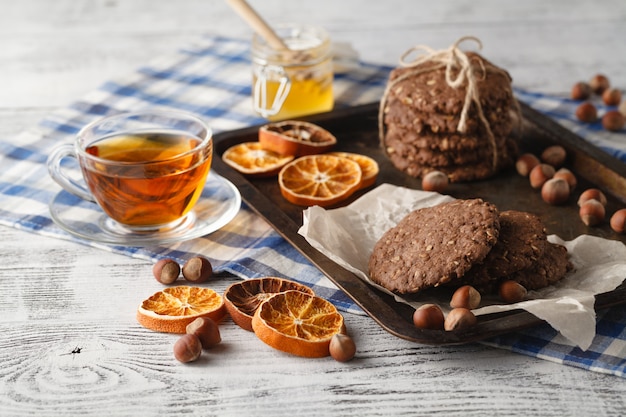 Fresh oat cookies with honey and cup of tea on white table