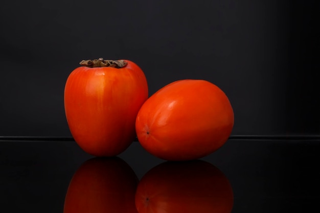 Fresh orange fruits of persimmon cultivar pyramid on black background with reflection