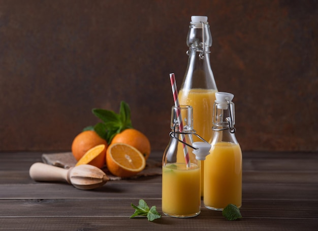 Fresh orange juice in three bottles with citrus fruits on  a brown wooden background. Rustic concept. Front view image