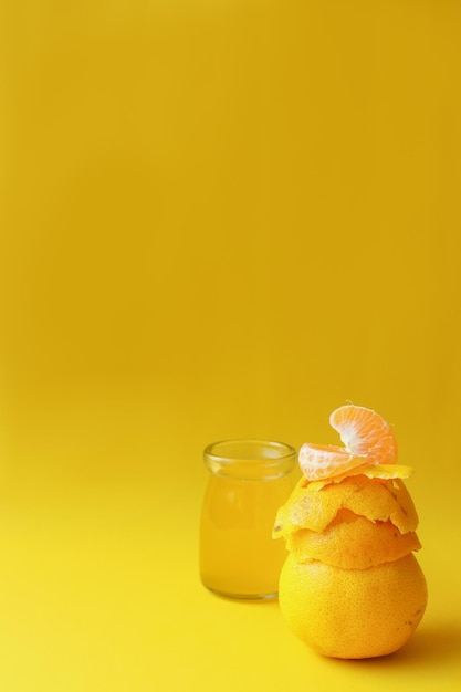 Fresh orange peels and slice fruit with blurred orange juice on yellow background with copy space