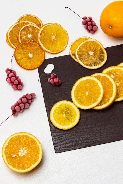 Fresh orange slices on brown board Sprigs of red frozen berries and dry orange slices on table