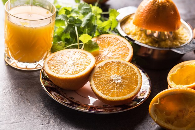 Fresh oranges juicer juice tropical fruits and herbs on concrete board.