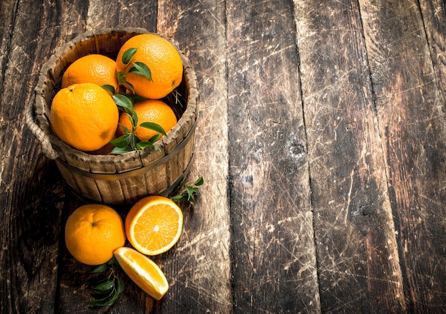 Fresh oranges in a wooden bucket. On a wooden background.