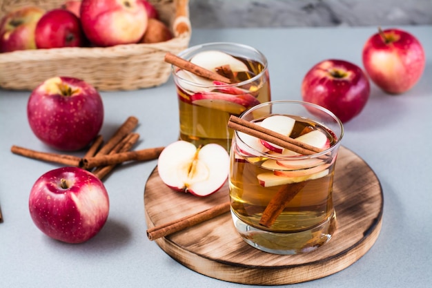 Fresh organic apple cider with cinnamon in glasses and apples on a gray background. Warming winter drinks