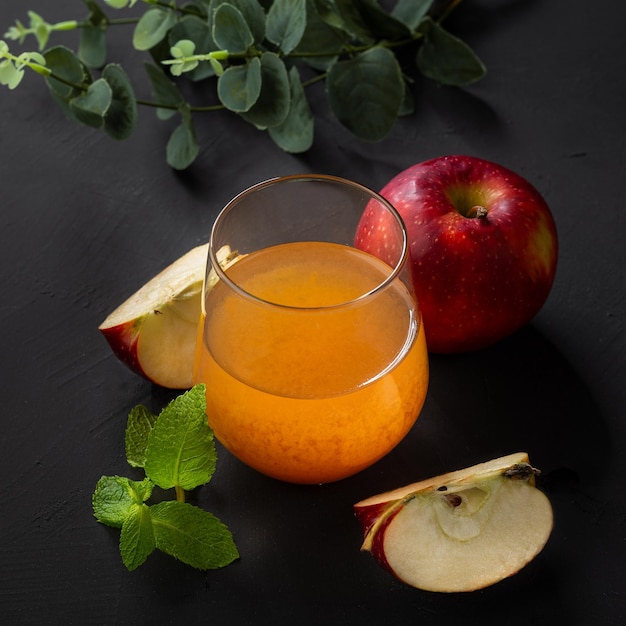 Fresh organic apple juice in a glass with raw whole and sliced red apples on black table