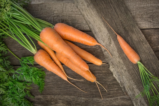 Fresh organic carrots with green tops on wooden table. Top view.