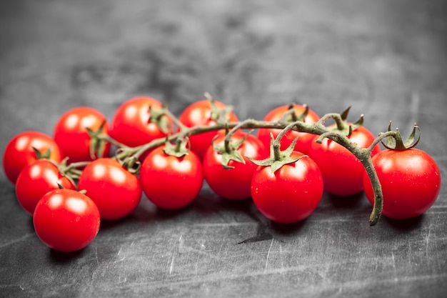 Fresh organic cherry tomatoes bunch closeup on black board.