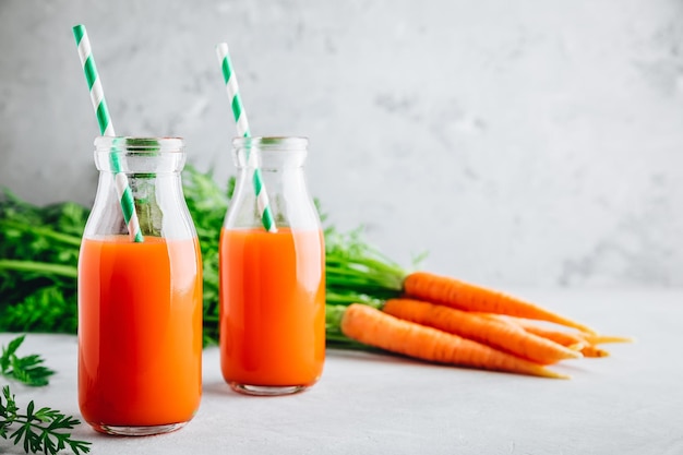 Fresh organic detox carrot juice in glass bottles on a gray stone background