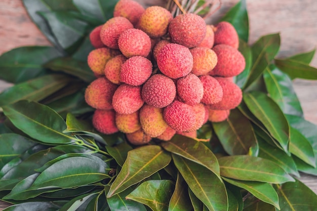 Fresh organic lychee fruit and lychee leaves on a rustic wooden surface