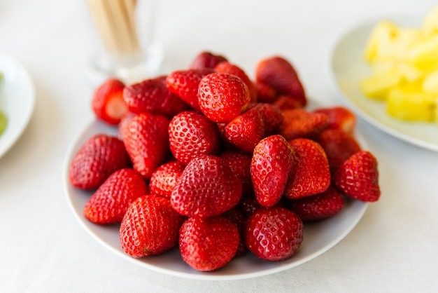 fresh organic natural red strawberries with green leaves over white background. circle made my different size sweet strawberries against white plate