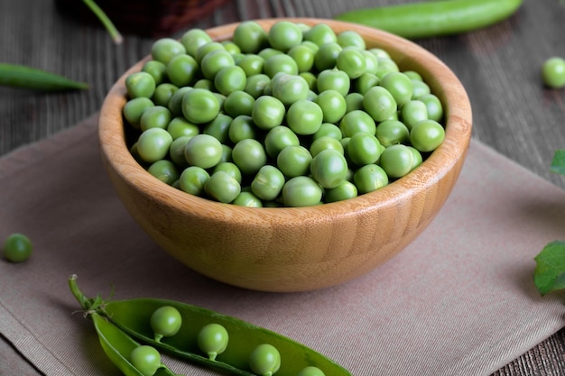 Fresh organic raw green peas in a bowl with peas plants leaves on dark wooden table background bean protein close up