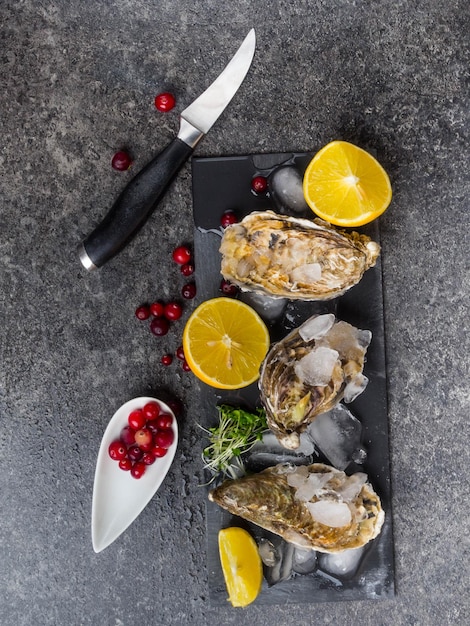 Fresh oysters in ice with lemon cranberries knife over stone table top view