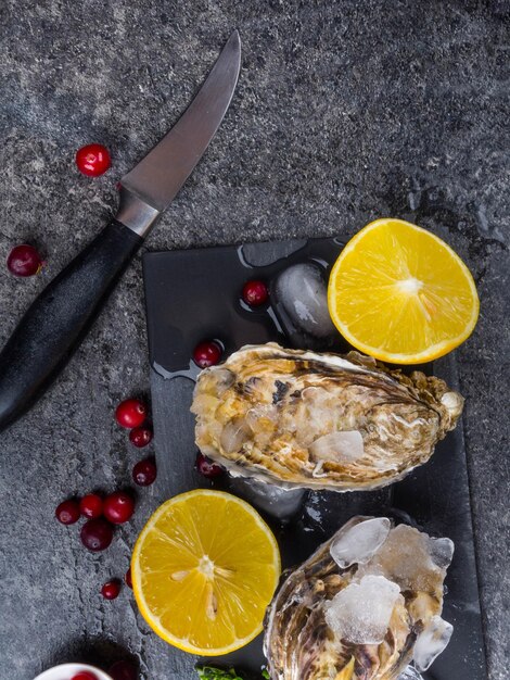 Fresh oysters in ice with lemon cranberries knife over stone table top view