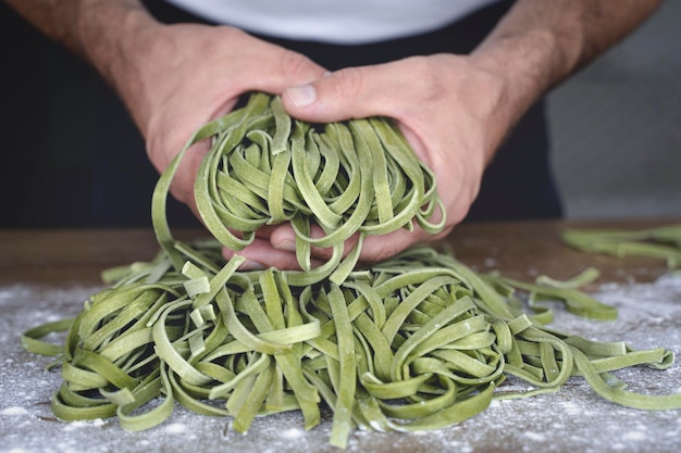 Photo fresh pasta homemade italian raw pasta fettuccine with spinach in the hands of the chef on the background of the kitchen