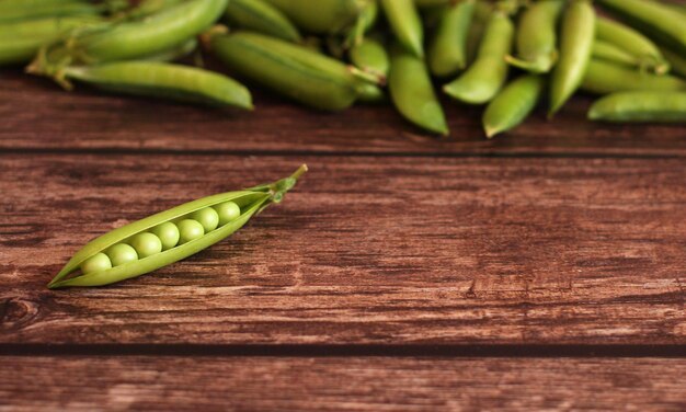 Fresh pea pod open with peas on a wooden background