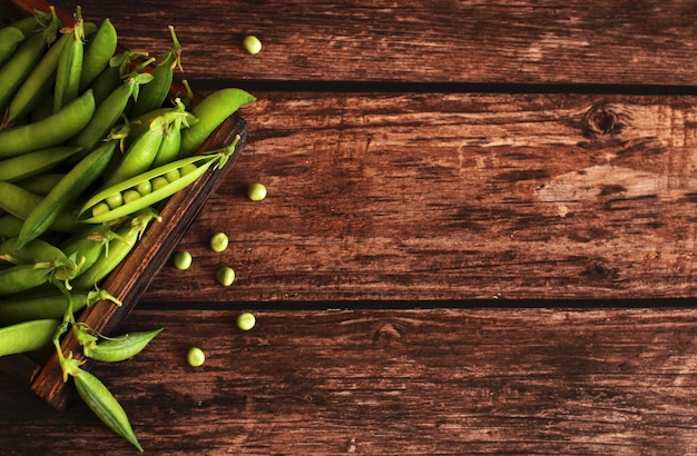 Fresh pea pods with peas in a wooden box on a wooden background