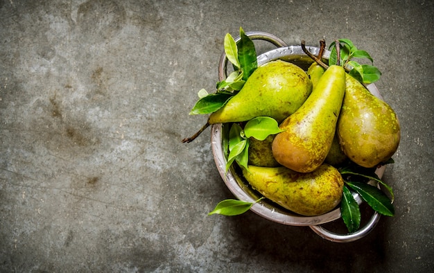 Fresh pears in the bowl with the leaves on the stone table. Top view