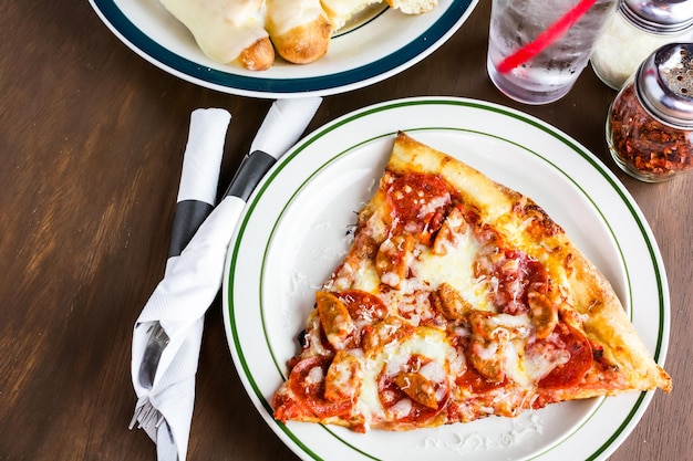 Fresh pepperoni and sausage pizza slice on the table in Italian restaurant.