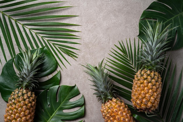 Fresh pineapple with tropical leaves on gray background