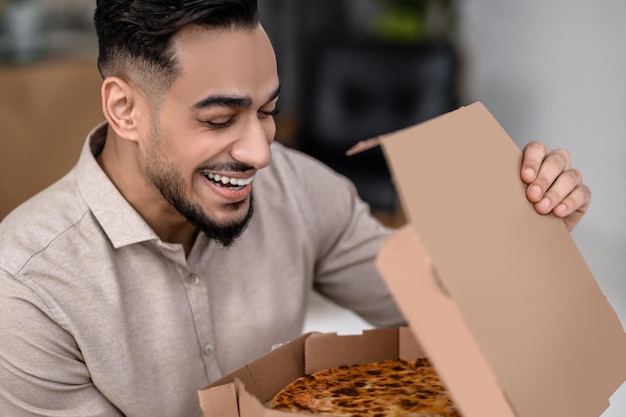 Fresh pizza. Close-up of a contented smiling face of young male with closed eyes holding open pizza box