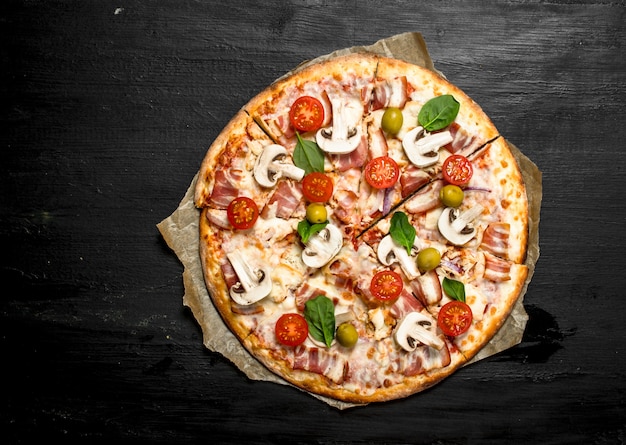 Fresh pizza with bacon, tomatoes, olives and greens. On the black chalkboard.