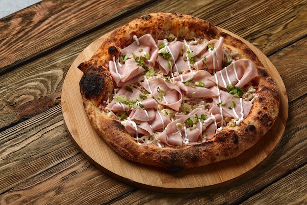 Fresh pizza with ham and pineapple on wooden table in restaurant