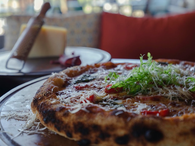 A fresh pizza with parmesan cheese in the background